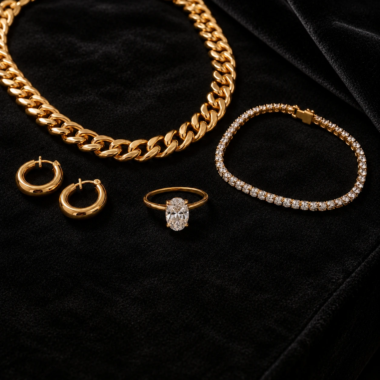 Gold Cuban chain, diamond tennis bracelet, oval solitaire ring and gold hoop earrings on black velvet